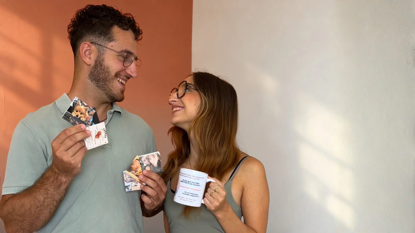 Aurélien et Chloé, souriants, tenant un mug photo personnalisé et des tirages de leurs souvenirs